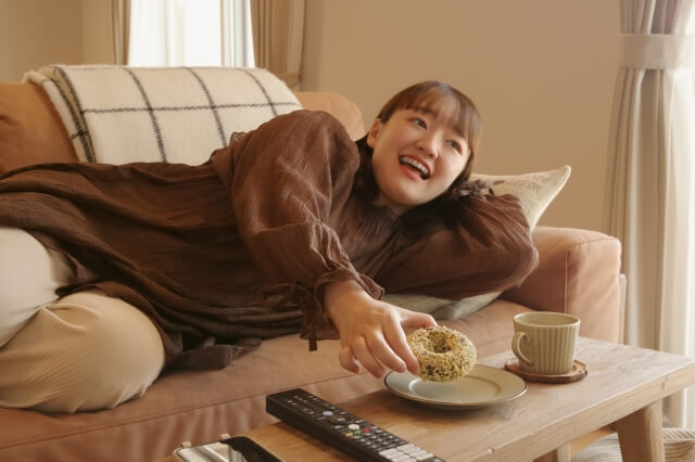 ソファに寝転がりながら間食する女性