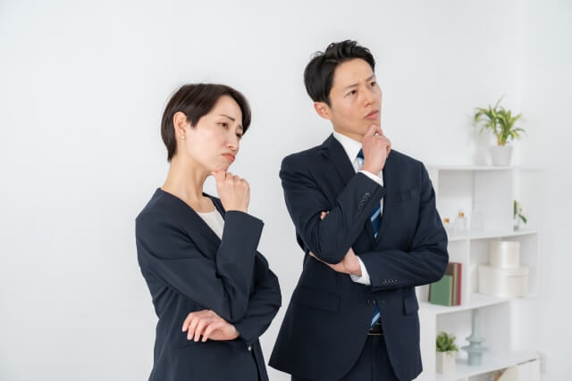 首をかしげるスーツを着た男女